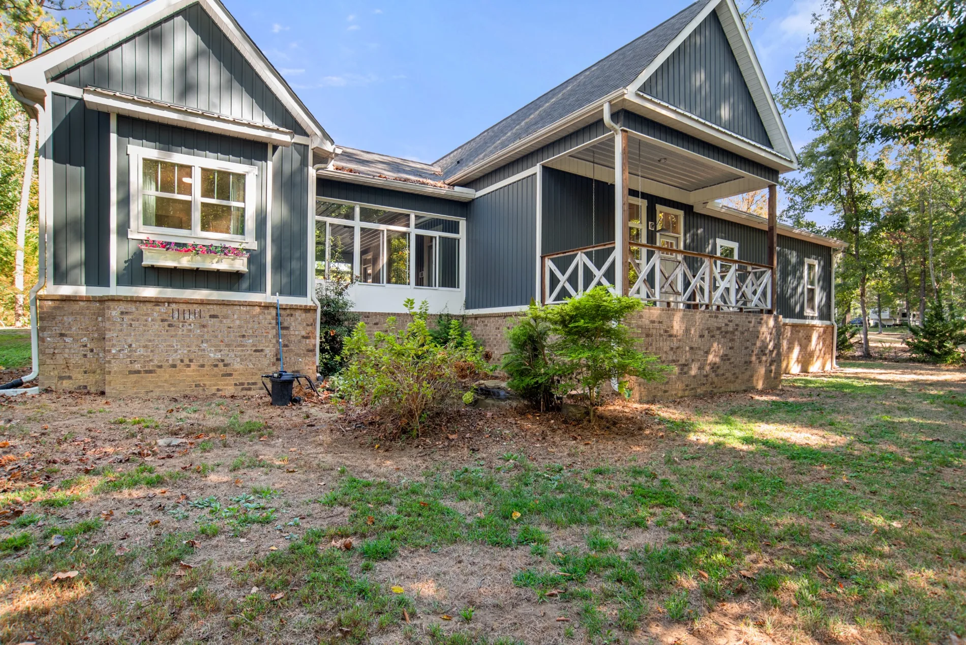Side exterior of charcoal-gray house with covered porch and landscaping