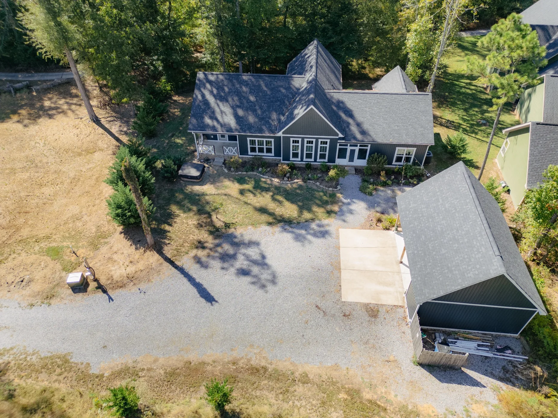 Drone view of charcoal-colored house with detached garage surrounded by trees